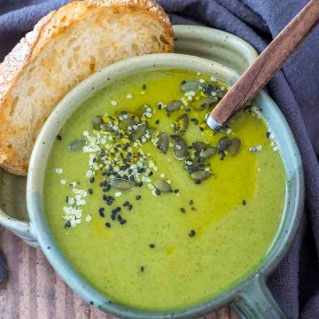 Creamy broccoli soup served in a bowl with a slice of bread, topped with pumpkin seeds.
