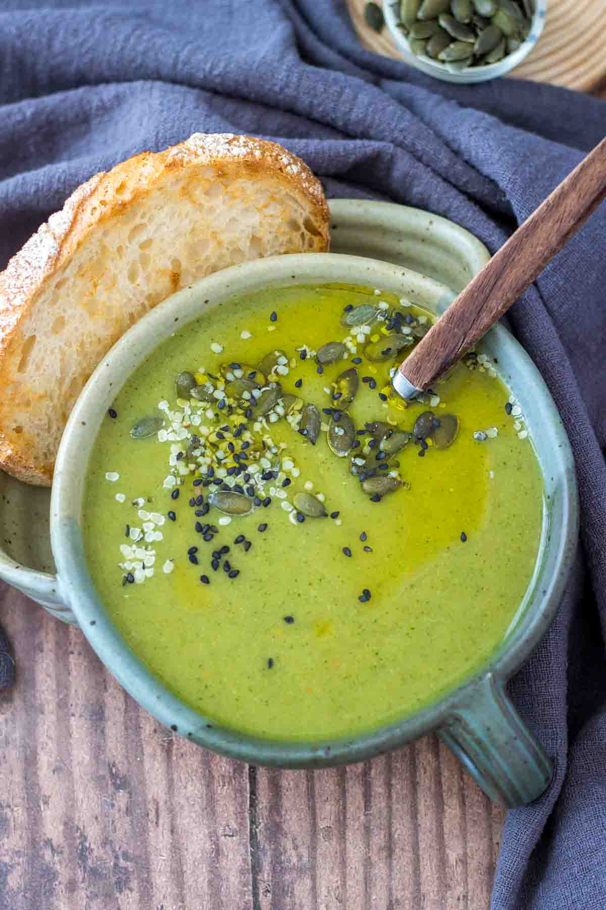 Creamy broccoli soup served in a bowl with a slice of bread, topped with pumpkin seeds.