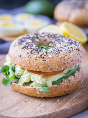Healthy mayo-free Avocado Egg Salad served with fresh veggies in a whole-grain bagel