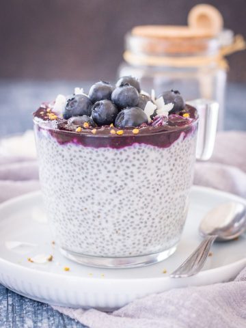 Blueberry Coconut Chia Pudding made with coconut cream topped with blueberry sauce, fresh blueberries, and coconut chips served in a glass bowl.