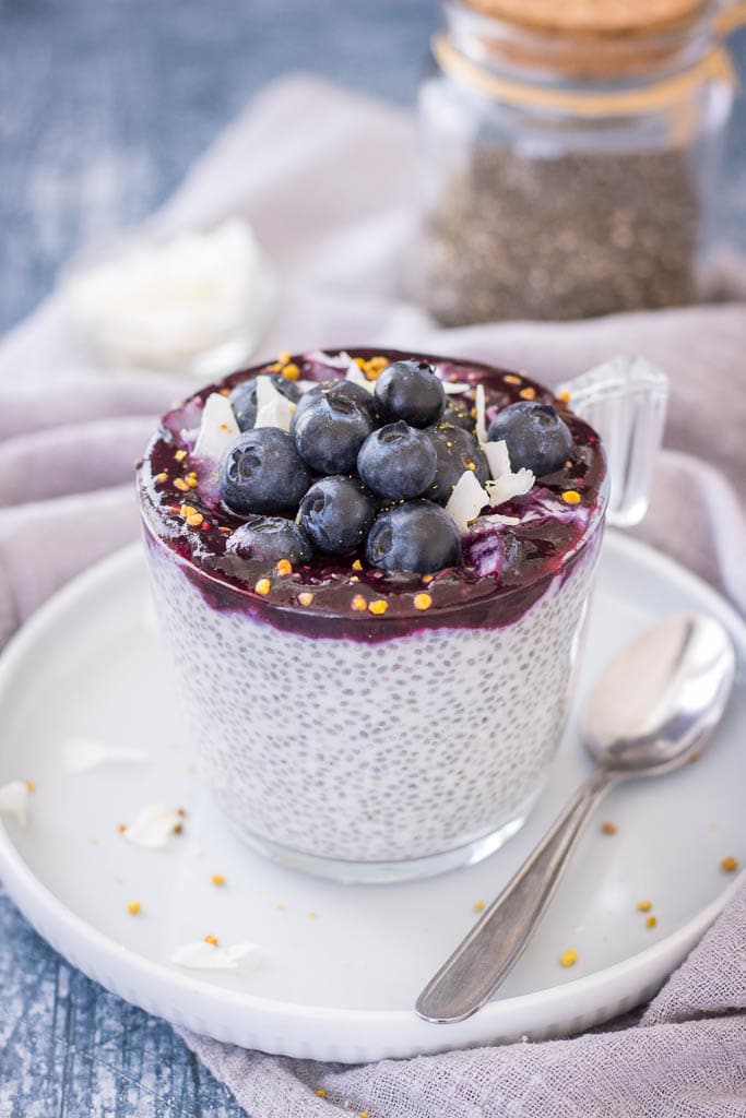 Blueberry Coconut Chia Pudding made with coconut cream topped with blueberry sauce, fresh blueberries, and coconut chips served in a glass bowl.