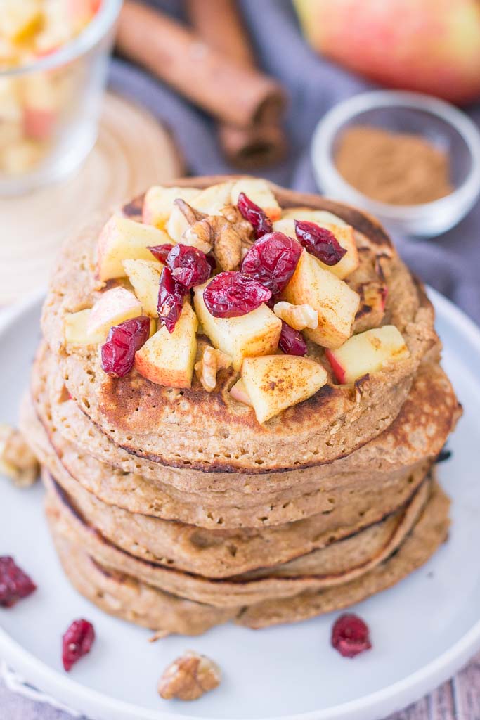 Stacked Apple Oatmeal Pancakes topped with diced apple, walnuts, and dried cranberries served on a plate