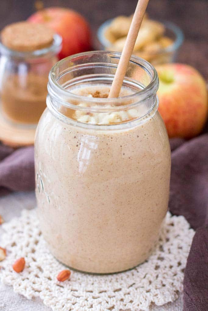 Smoothie aux pommes et au beurre d'arachide servi avec une paille dans un bocal en verre garni de beurre d'arachide crémeux et d'arachides concassées