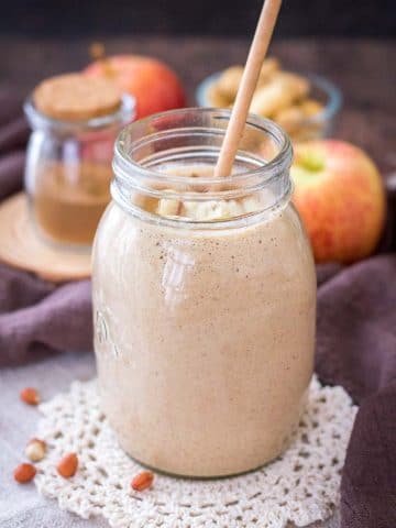 Apple Peanut Butter Smoothie served with a straw in a glass jar topped with creamy peanut butter and crushed peanuts