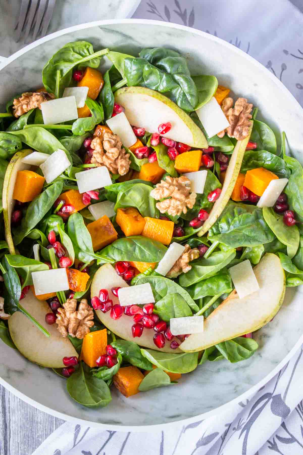 Pumpkin Pear Salad with baby spinach and walnuts topped with cheese and seeds served in a bowl
