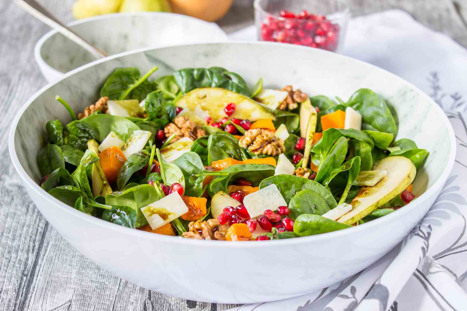 Pumpkin Pear Salad with baby spinach and walnuts topped with cheese and seeds served in a bowl