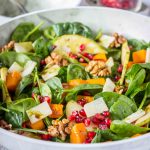 Pumpkin Pear Salad with baby spinach and walnuts topped with cheese and seeds served in a bowl