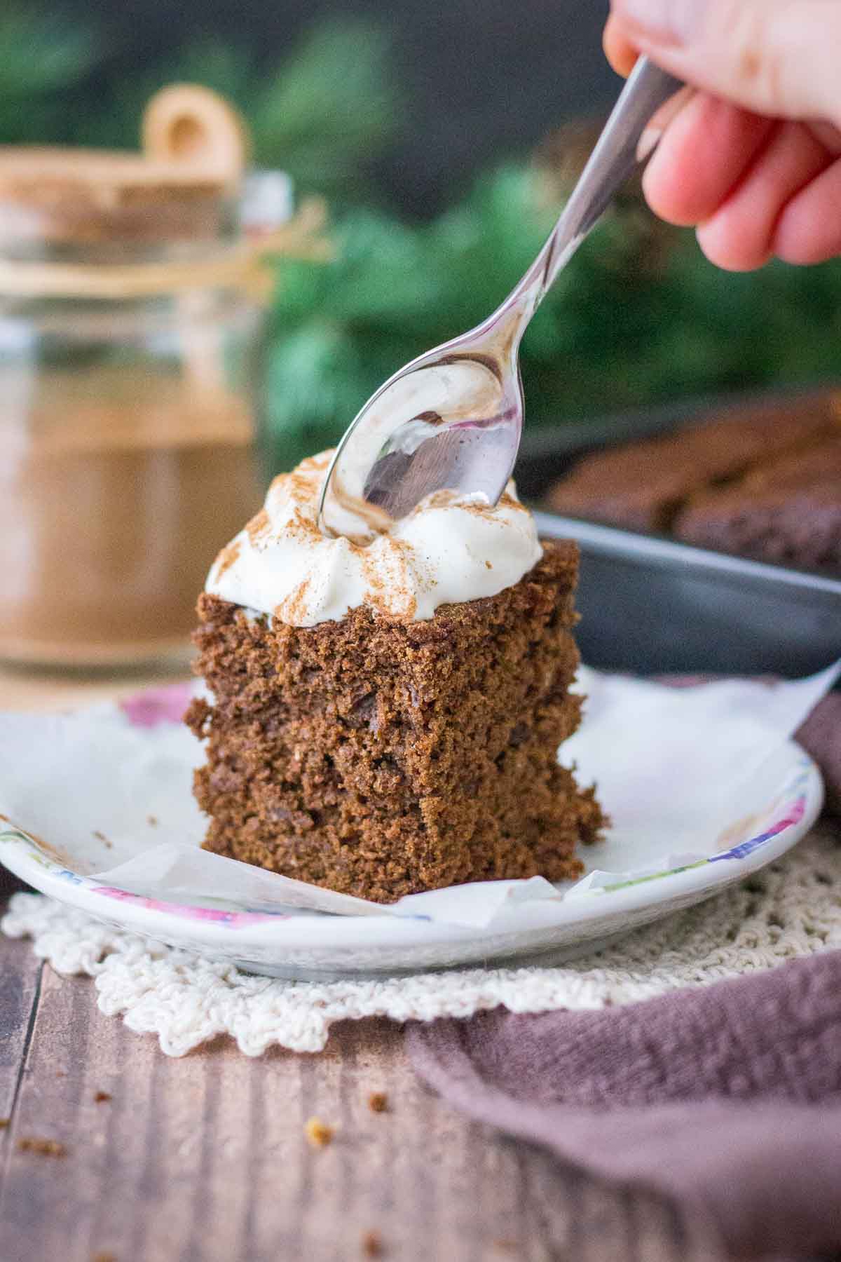 A slice of Gingerbread Cake topped with whipped cream served on a plate