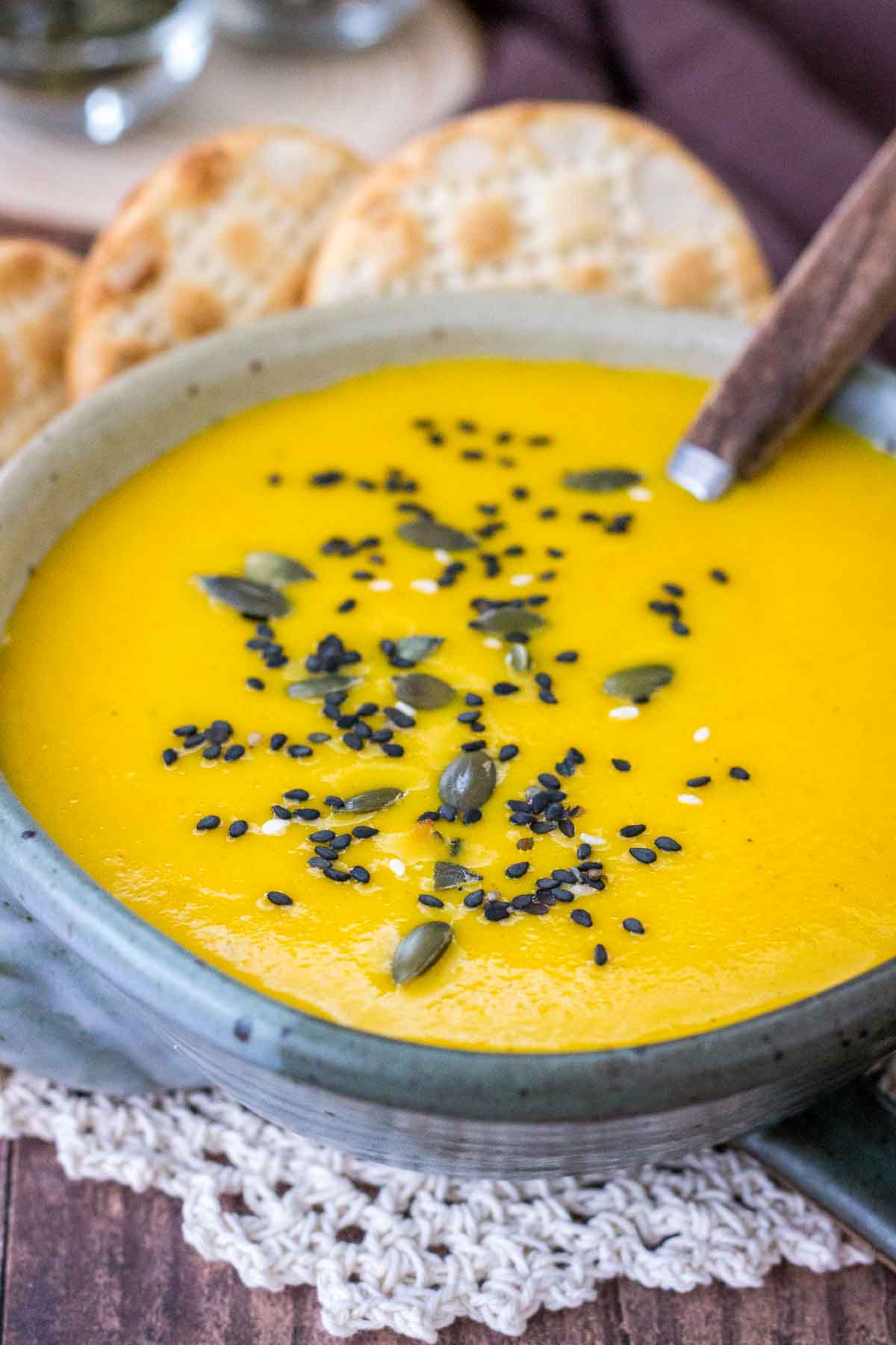 Creamy curry carrot soup served in a bowl with crackers topped with seeds