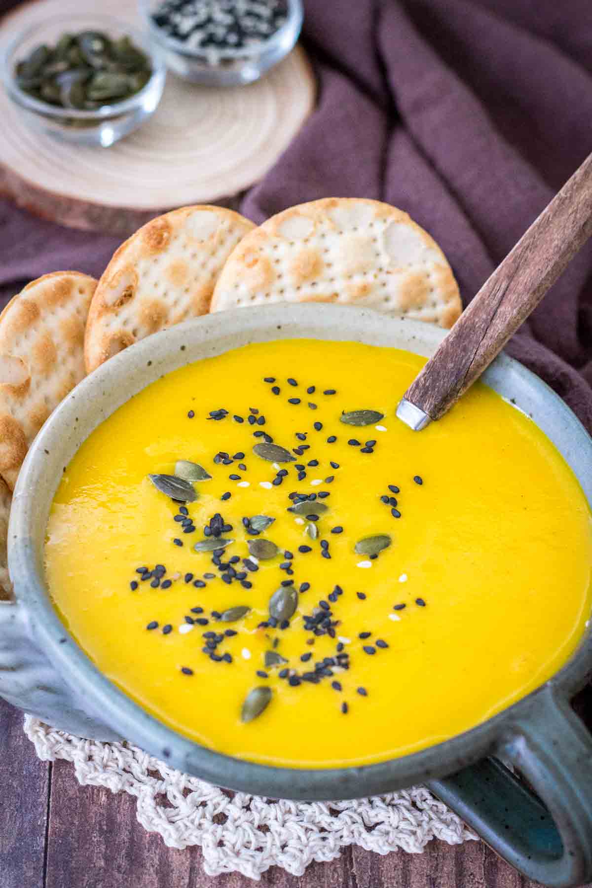 Creamy carrot curried soup served in a bowl with crackers topped with seeds