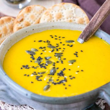Creamy Carrot Curry Soup served in a bowl with crackers topped with seeds