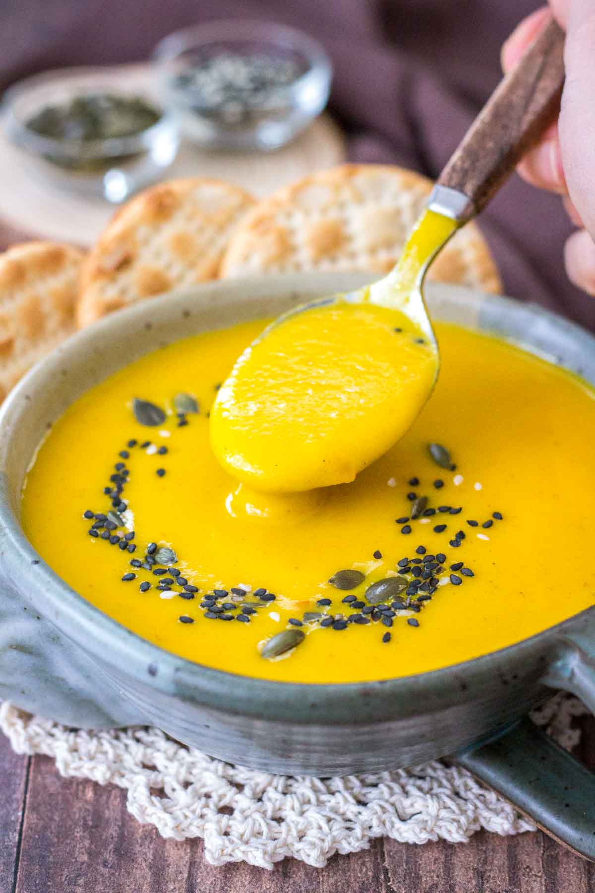Creamy Carrot Soup served in a bowl with crackers topped with seeds