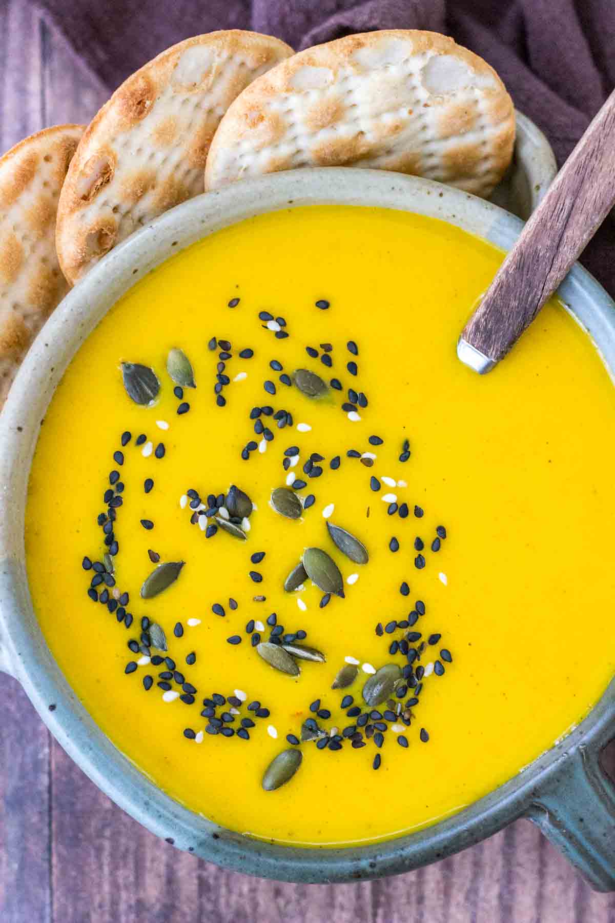 Creamy Carrot Curry Soup served in a bowl with crackers topped with seeds