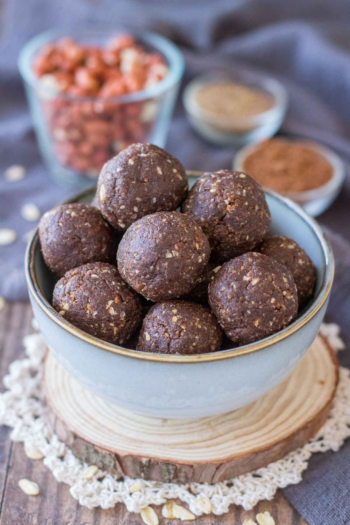 Chocolate protein balls served in a small bowl, spices and raw peanuts in a background