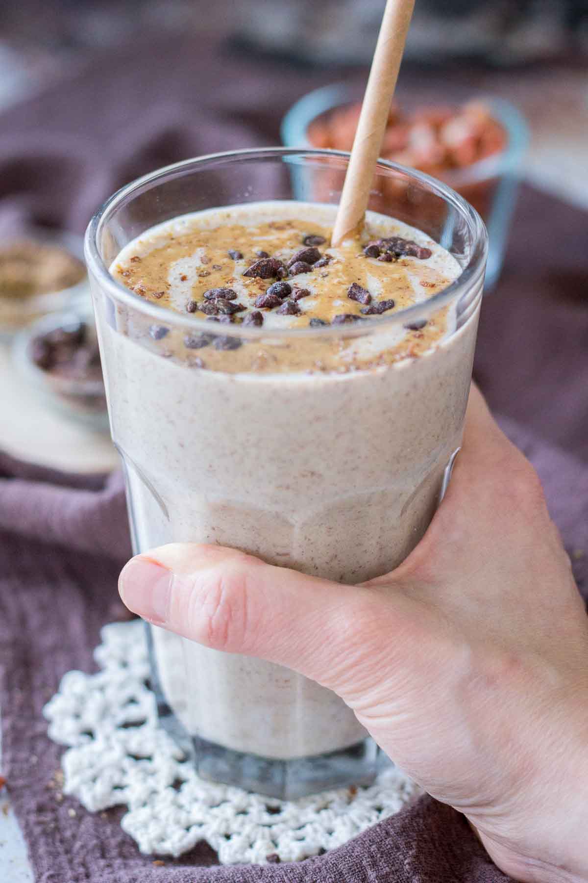 Hand holding a Peanut Butter Protein Shake topped with peanut butter and chocolate served in a glass with a straw