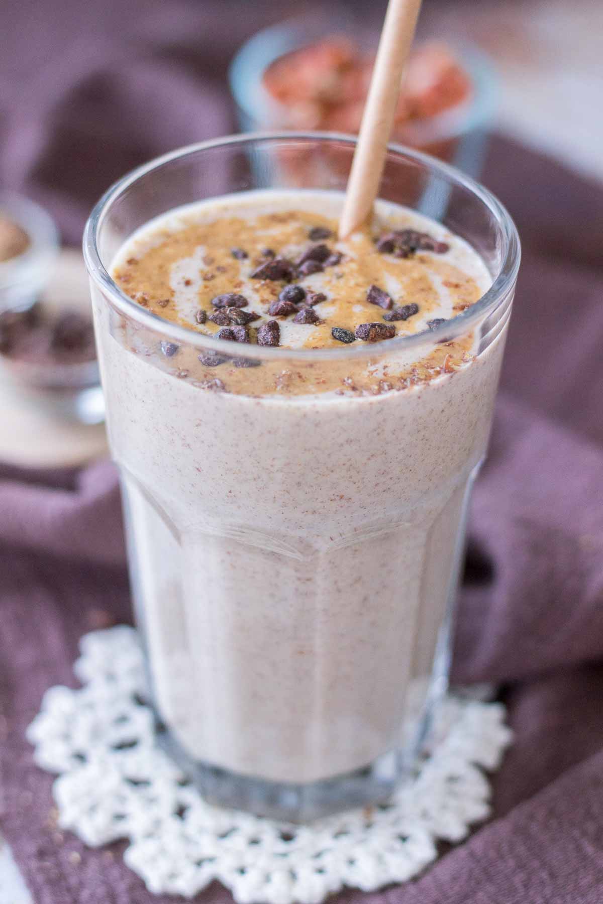 Close up of a Peanut Butter Protein Shake in a glass topped with peanut butter and chocolate with a straw
