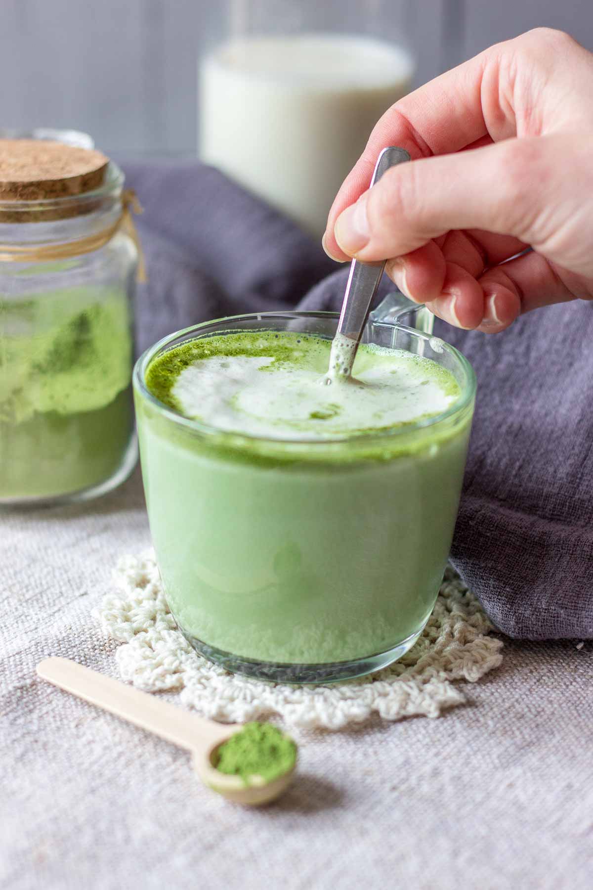 Hand mixing a matcha green tea latte served in a mug