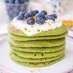Matcha green tea pancakes served on a plate topped with fruits.