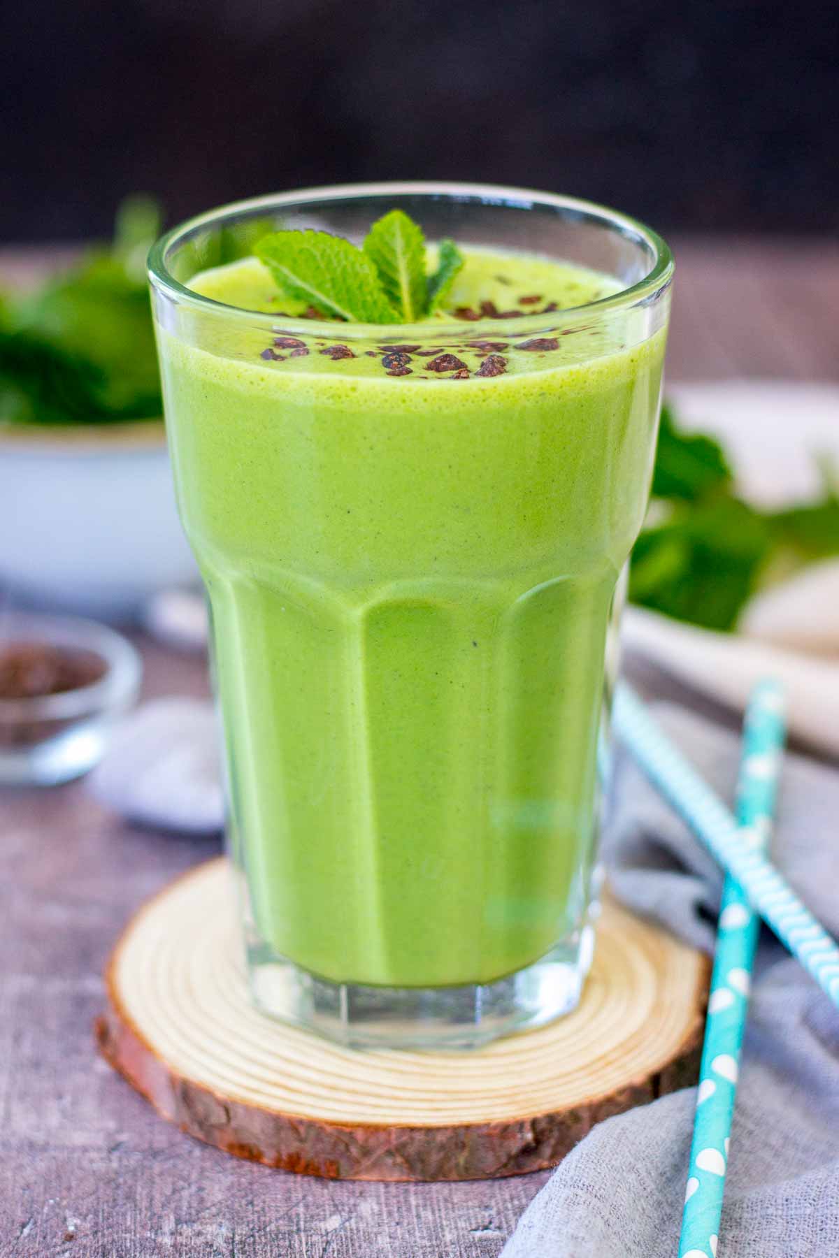 Shamrock protein shake served in a glass, topped with chocolate chips and fresh mint.