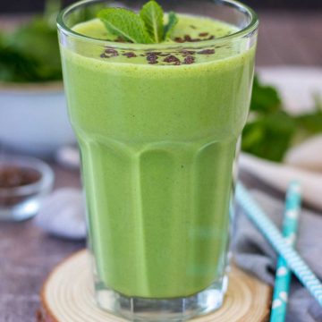 Shamrock protein shake served in a glass, topped with chocolate chips and fresh mint.