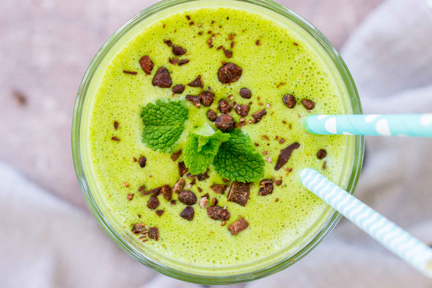 Upper view of a shamrock protein shake served in a glass with two colorful straws.
