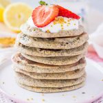 Lemon Poppy Seed Pancakes served on a plate topped with yogurt and strawberries.