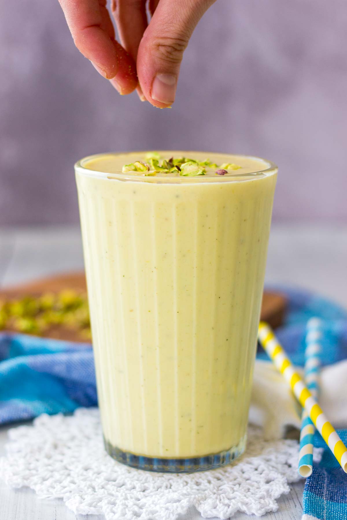 hand putting crushed pistachio on Mango Lassi