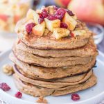 Apple Oatmeal Pancakes stacked on a plate topped with diced apples and cranberries