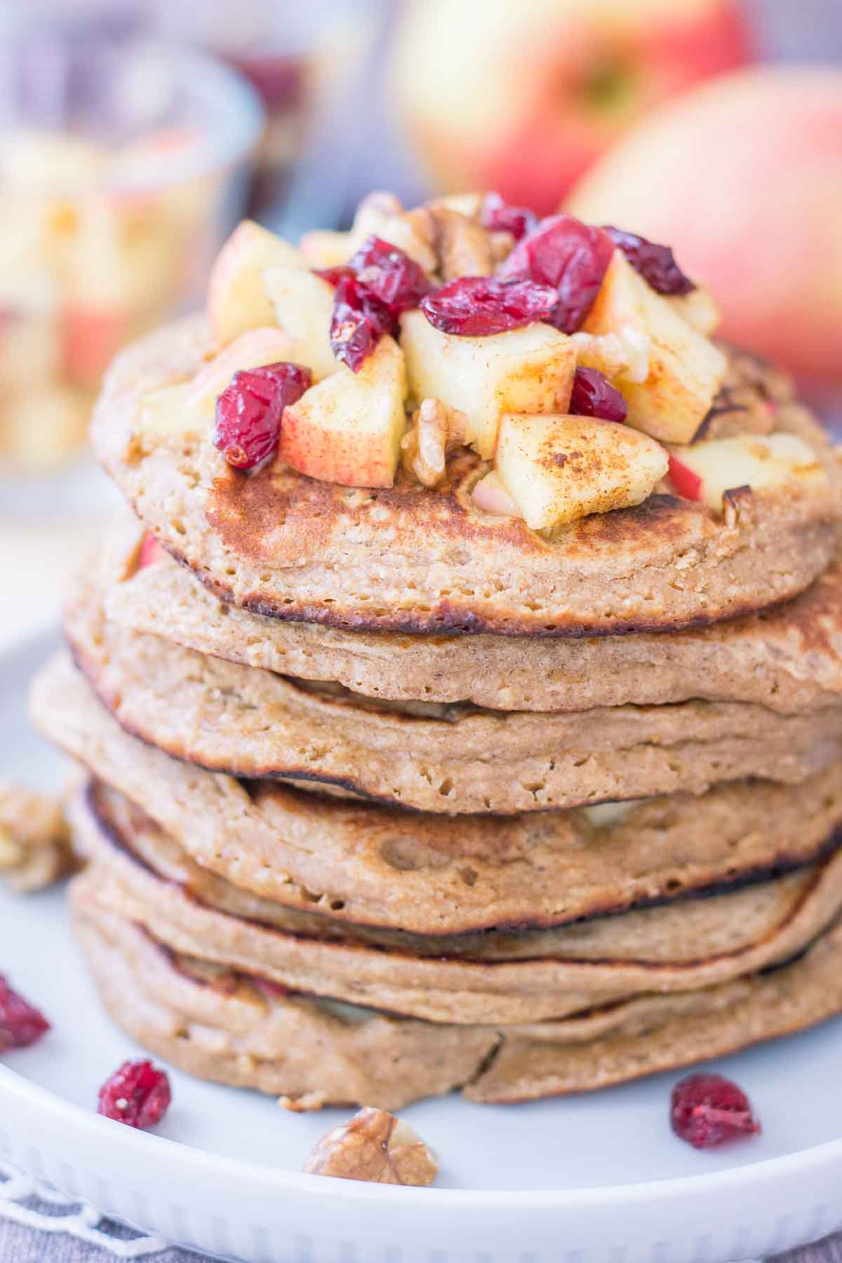 Apple Oatmeal Pancakes stacked on a plate topped with diced apples and cranberries