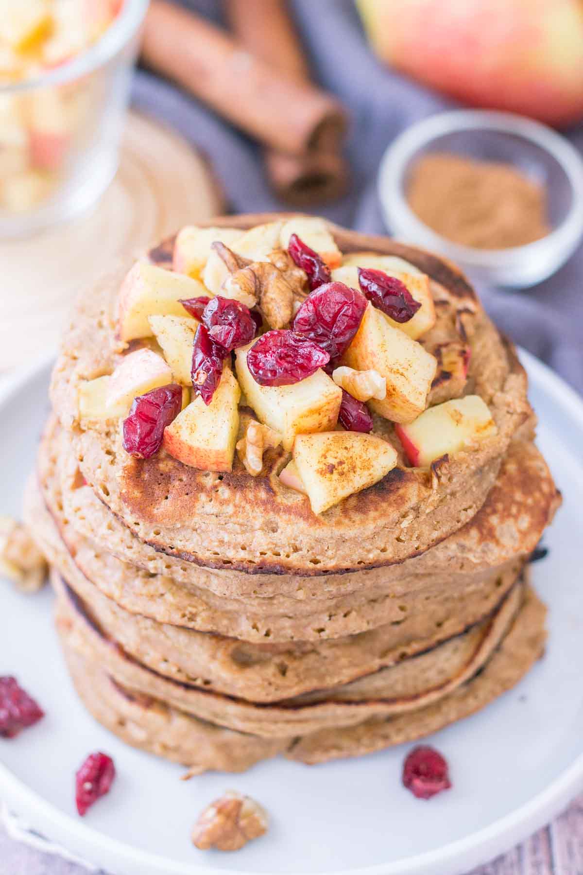 Apple Oatmeal Pancakes stacked on a plate topped with diced apples and cranberries