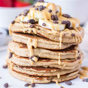 Peanut Butter Oatmeal Pancakes stacked on a plate topped with slices of banana and chocolate