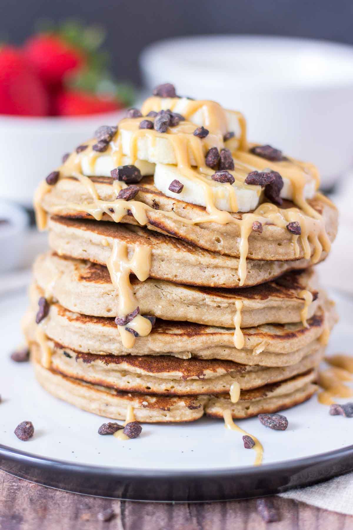 Peanut Butter Oatmeal Pancakes stacked on a plate topped with slices of banana and chocolate