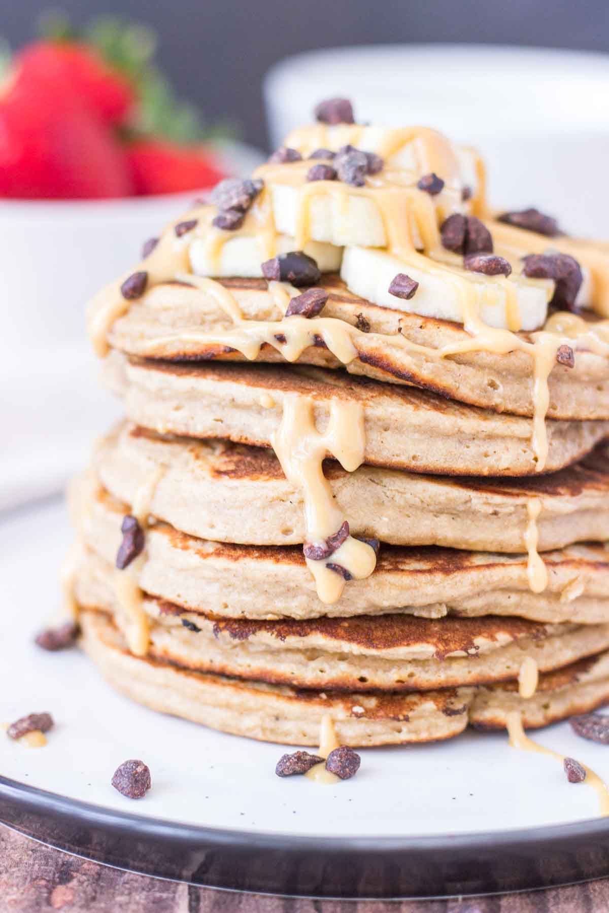 Peanut Butter Oatmeal Pancakes stacked on a plate topped with slices of banana and chocolate