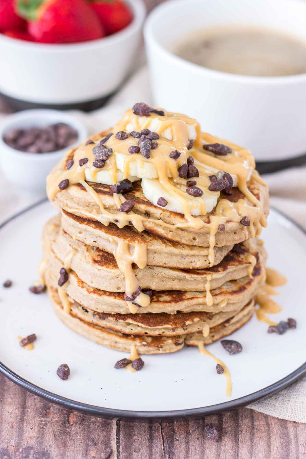 Peanut Butter Oatmeal Pancakes stacked on a plate topped with slices of banana and chocolate