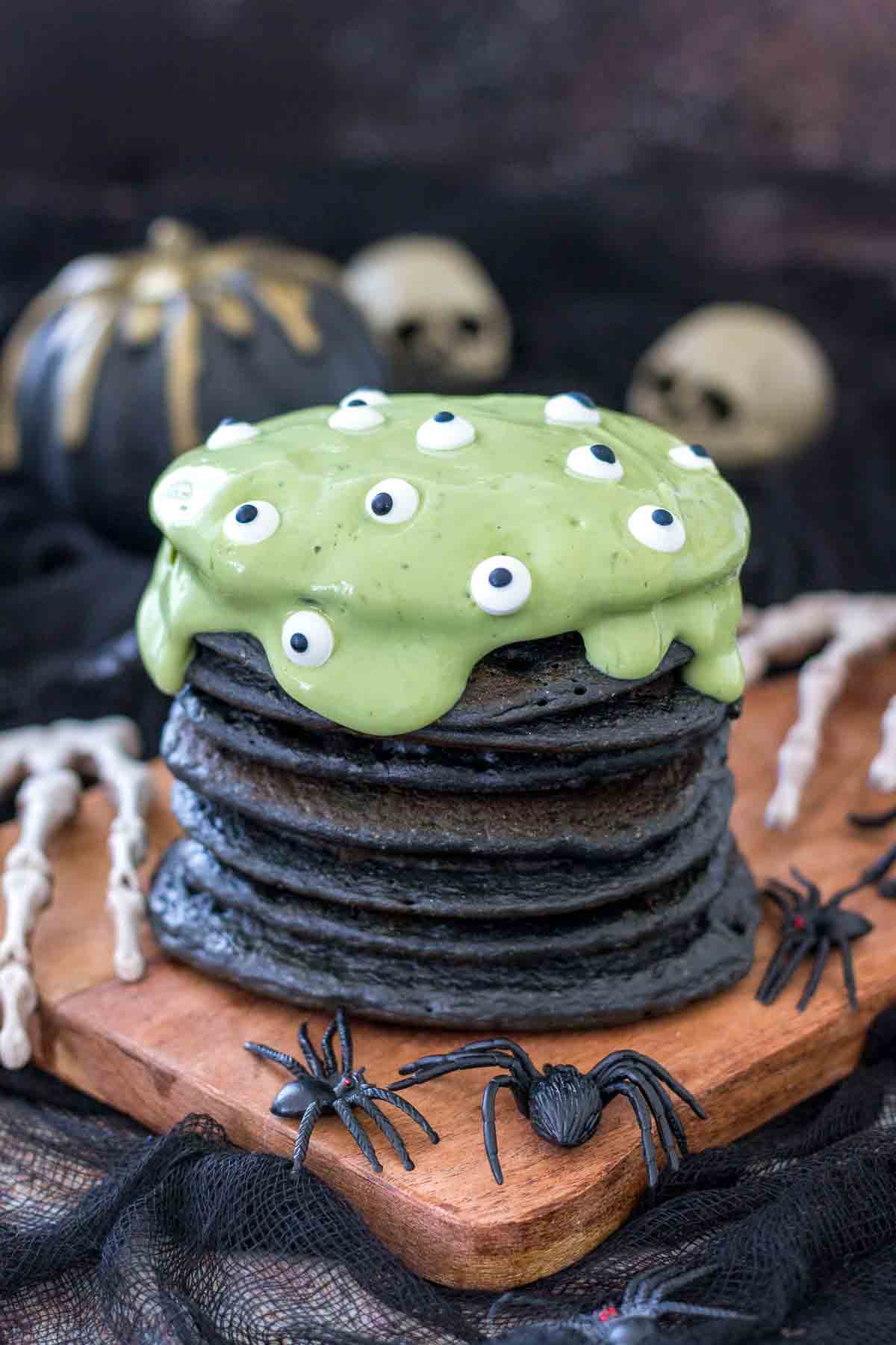 Halloween Pancakes placed on a wooden plate surrounded by spooky spiders