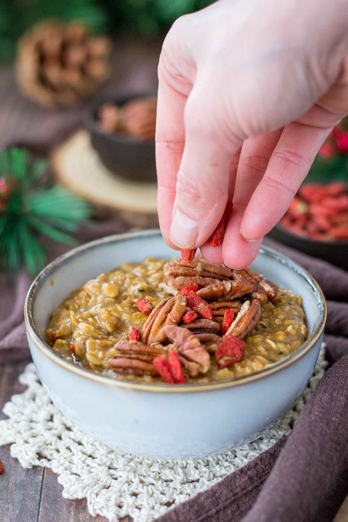 Hand putting goji berries on top of the Gingerbread Oatmeal
