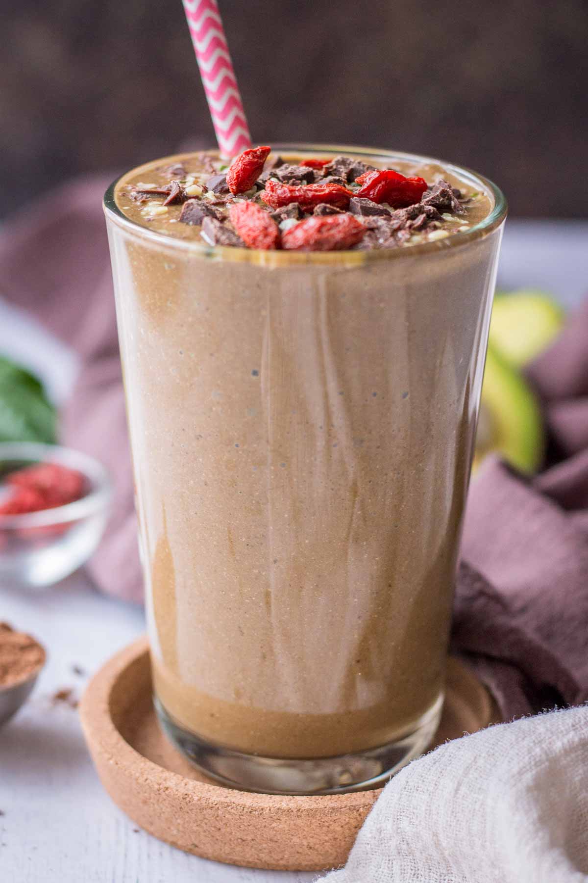 Chocolate banana avocado smoothie served in a smoothie glass topped with goji berries and chocolate